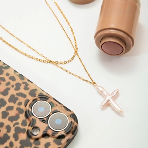 Collier multi-rangs doré avec perle d'eau douce en forme de croix sur fond blanc