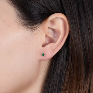 Close-up of a model wearing a small gold stud earring with a round green zircon stone