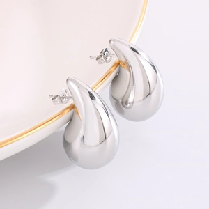 Macro detail of silver drop earrings with polished finish on a white ceramic plate