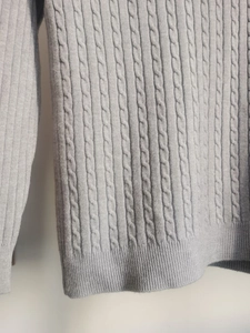 Dettaglio della trama a trecce grigie e del polsino elastico a coste del maglione