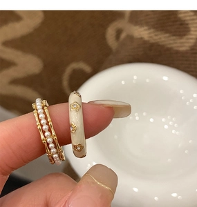 Detail view of pearl bamboo ring and cream enamel flower ring on finger with vintage aesthetic