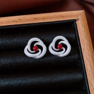 Detail shot of silver swirl hollow earrings with red beads on black velvet box