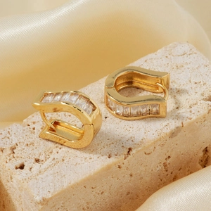 U-shaped gold plated earrings with zircon crystals on stone over golden silk fabric