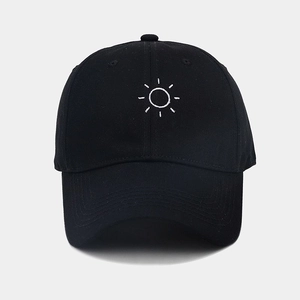 Close-up of white sun embroidery detail on a black soft top baseball cap with curved brim