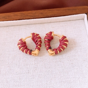 Macro view of 18k gold heart earrings with red woven texture in a wooden jewelry box