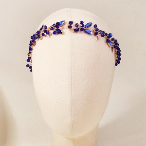 Close-up of handmade bridal headband with blue crystals and gold leaves on a mannequin