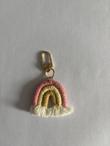 Detailed close-up of handmade rainbow keychain with pink yellow cotton weave and gold clasp