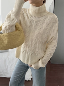 Women's off-white turtleneck cable knit sweater in cozy indoor bedroom setting