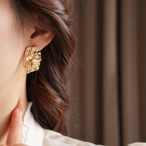 Detailed close-up of golden irregular wrinkled earrings on a model with metallic texture