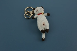 Detail of handmade crochet Siamese cat keychain with white yarn and golden bell accessory