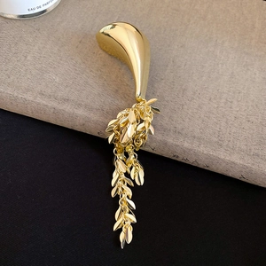 Macro detail of golden geometric leaf tassel brooch on dark book and black fabric