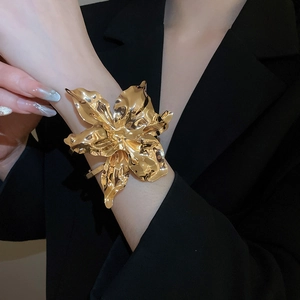 Close-up of oversized gold flower cuff bracelet on black blazer with metallic texture