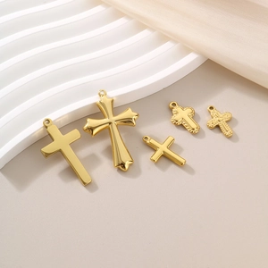 Five assorted gold titanium steel cross pendants displayed on an elegant white pedestal