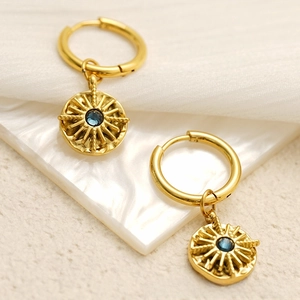 Detail of gold-plated stainless steel hoop earrings with sunburst charms and blue stones
