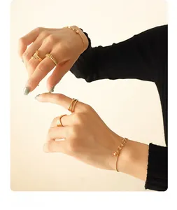Detail of layered gold-plated steel chain bracelet with small bead charms and rings
