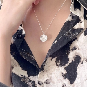 Detail of a round textured S925 sterling silver compass pendant necklace on a model's neck
