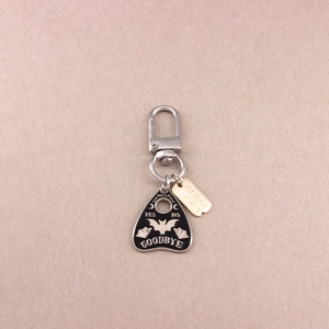 Macro shot of silver Ouija planchette pendant keychain with engraved gold Harmony tag