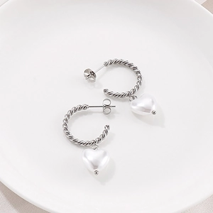 Détail de boucles d'oreilles créoles torsadées argentées avec pendentif perle en cœur
