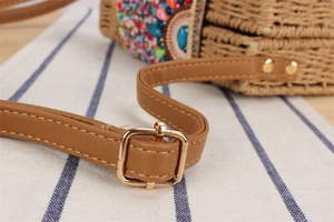 Détail de la bandoulière en cuir PU marron avec boucle dorée sur un sac en paille