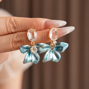 Detail of blue flower earrings with oval gemstones and small pearls held in hand