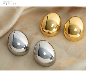 Macro shot of oval gold and silver polished hoop earrings on elegant beige silk fabric