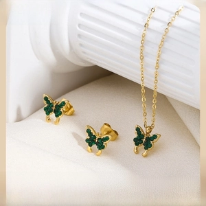 Detailed macro view of golden butterfly necklace and earrings with emerald green crystals