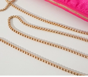 Detail of fuchsia pleated satin fabric with a luxury gold metal bead chain strap