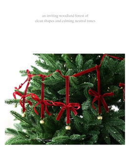 Close-up of red velvet bows with gold bells hanging on a green Christmas tree branch