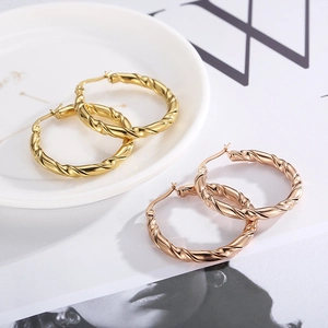 Dettaglio macro di orecchini a cerchio intrecciati oro e oro rosa su ceramica bianca
