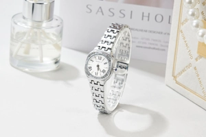 Close-up of square silver watch dial with Roman numerals, crystal bezel and blue gem crown