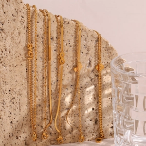 Detail of golden stainless steel bracelets with charms on a textured stone surface