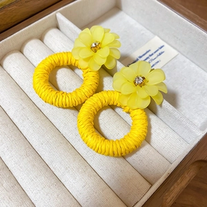 Macro shot of yellow resin flower earrings with woven straw hoops in a jewelry box