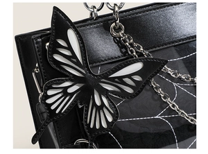 Detail of black ita bag featuring a monochrome butterfly charm and silver metal chain strap