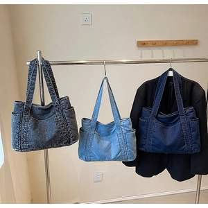 Three denim tote bags in dark grey, light blue, and dark blue hanging on a metal rack