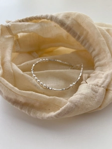 Detailed close-up of S925 sterling silver pearl bracelet on a cream linen pouch background