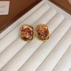 Detail shot of amber resin square earrings with gold metal frame on a beige jewelry tray