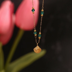Macro shot of gold shell pendant necklace with faceted green beads on a fine chain