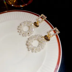 Elegant gold pearl and zircon square drop earrings displayed on a white ceramic plate