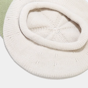 Makrodetail der weichen Stricktextur und Rollkante an einer cremeweißen Wollbaskenmütze