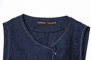 Detail von Rundhalsausschnitt und Metallknopf an dunkelblauer Denim-Weste mit Leinentextur