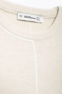 Close-up of the beige knit sweater neckline showing the brand label and size information