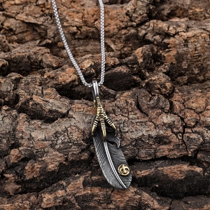 Collana con ciondolo artiglio d'aquila e piuma in oro e argento su sfondo di corteccia