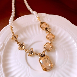 Detail of champagne crystal pendants and white pearls on a gold necklace over ceramic