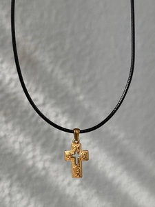 Detailed close-up of 18k gold-plated cross pendant with textured engraving and black cord
