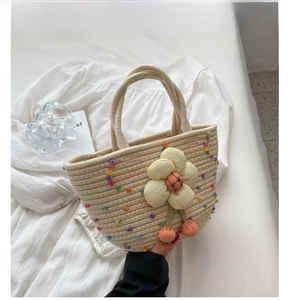 Close-up of cream woven handbag with 3D floral accents and colorful pom-poms