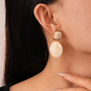 Close-up of beige marbled resin earrings with gold edges on model's ear