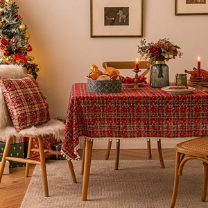 Red plaid Christmas tablecloth with pom-pom tassels in a cozy festive dining scene
