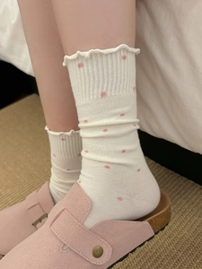 Detail of white ruffle socks with pink polka dots paired with pink slippers in cozy home setting