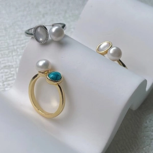 Close-up of pearl and turquoise rings displayed on a white wavy jewelry stand