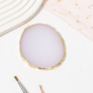 Detail of pink resin agate nail palette with gold rim edge on a white desktop